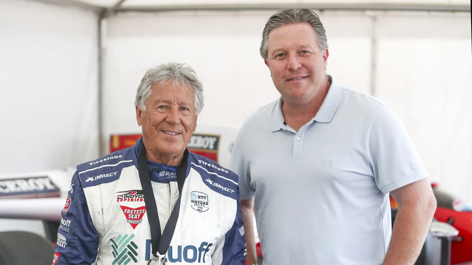 Зак Браун (вдясно) с Марио Андрети на Goodwood Festival of Speed през юли 2021 г. — архивна снимка, не от Сингапур 2026. United Autosports / Wikimedia Commons, CC BY-SA 2.0; изрязано до 16:9; производното остава под CC BY-SA 2.0. Оригинал: https://commons.wikimedia.org/wiki/File:AndrettiBrown-02_(51305826212).jpg ; лиценз: https://creativecommons.org/licenses/by-sa/2.0/