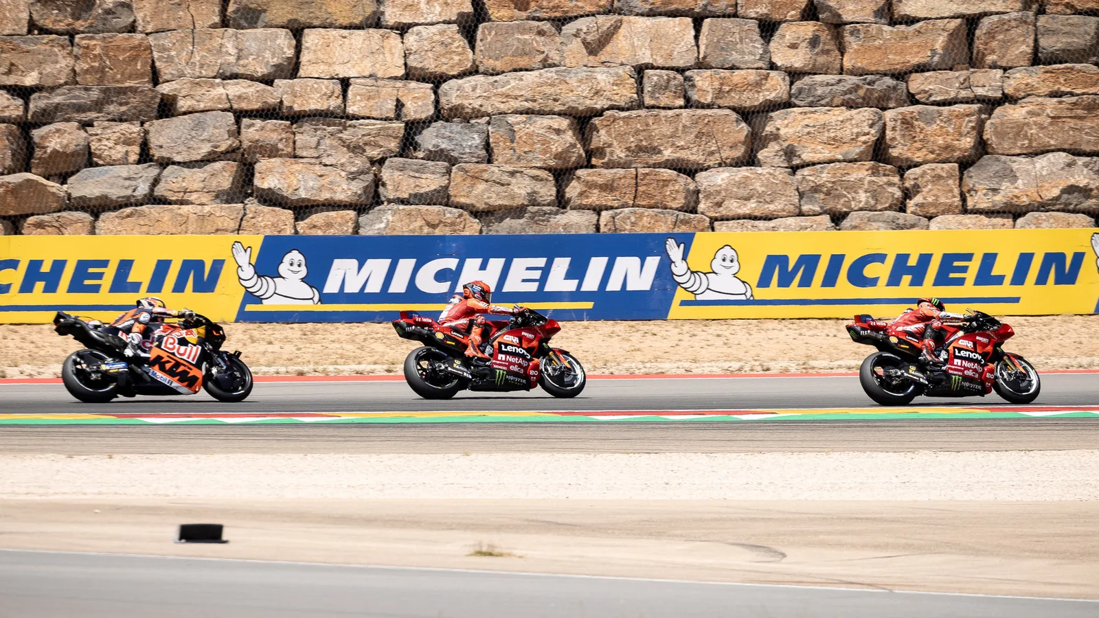 Архив: Марк Маркес с Ducati №93 между Франческо Баная и Педро Акоста на Гран при на Арагон 2025; не е кадър от отменения старт в Австралия 2026. TeamEG00 / Wikimedia Commons, public domain. Оригинал: https://commons.wikimedia.org/wiki/File:Francesco_Bagnaia,_Marc_M%C3%A1rquez,_and_Pedro_Acosta_during_the_2025_Aragon_motorcycle_Grand_Prix.jpg ; изрязано и оразмерено до 16:9 без AI редакция.