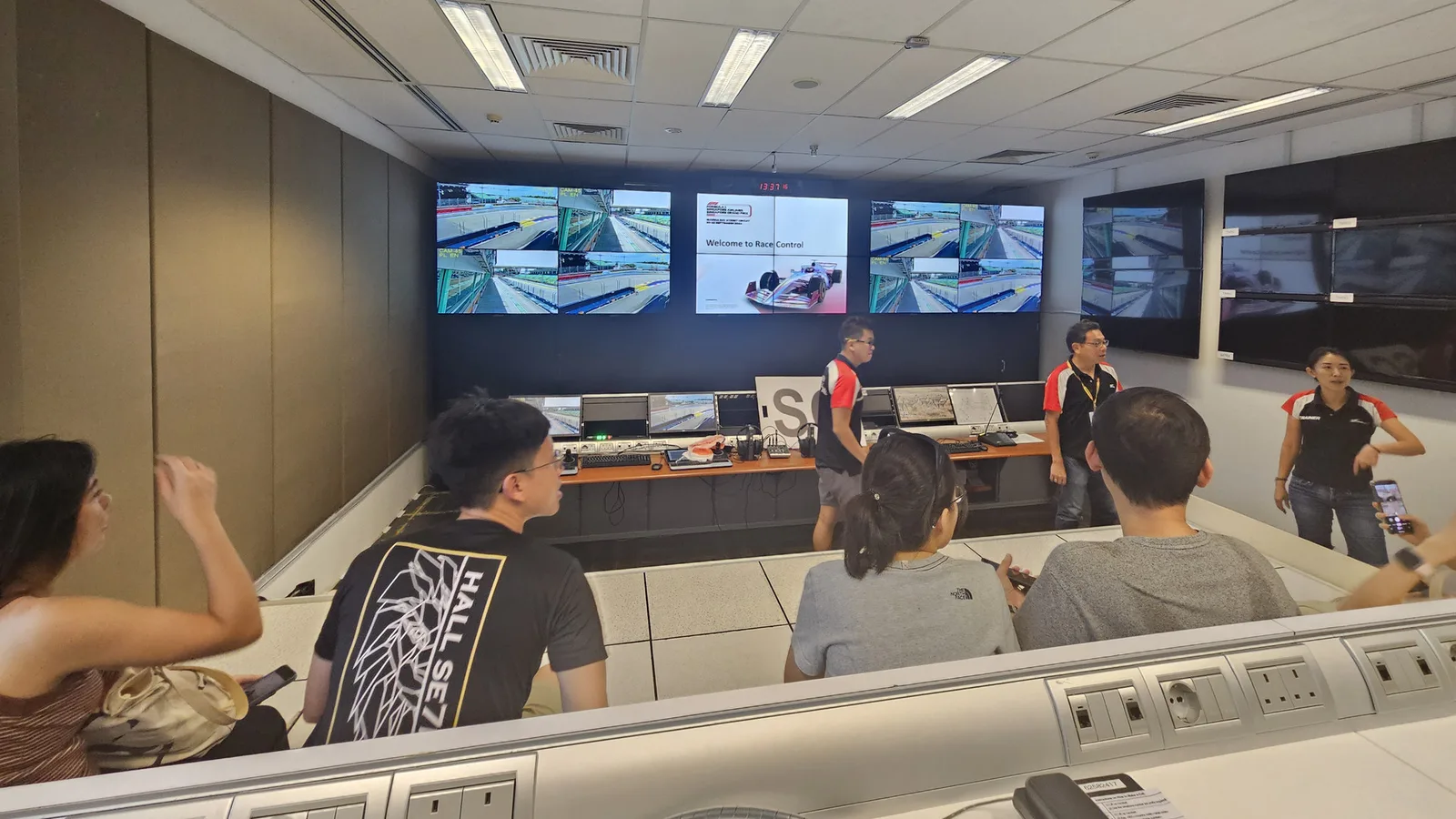 Архив: състезателният контрол на Marina Bay Street Circuit в Сингапур, 18 август 2024 г., по време на посещение; не е кадър от оперативния център в Бигин Хил или от работата на екипа през 2026 г. Asalover2004 / Wikimedia Commons, CC BY-SA 4.0. Изрязано и оразмерено до 1920×1080 без AI редакция; адаптацията остава под CC BY-SA 4.0. Оригинал: https://commons.wikimedia.org/wiki/File:Race_Control_Room_-_Singapore_Grand_Prix.jpg ; лиценз: https://creativecommons.org/licenses/by-sa/4.0/