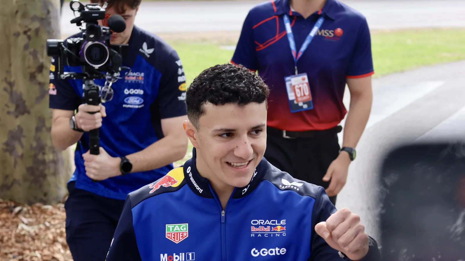 Исак Хаджар с екип на Ред Бул на Melbourne Walk преди Гран при на Австралия през март 2026 г. — архивен кадър, не от Сепанг. Yu Chu Chin / Wikimedia Commons, CC BY-SA 4.0; изрязано до 16:9. Оригинал: https://commons.wikimedia.org/wiki/File:Isack_Hadjar_at_the_Melbourne_Walk_during_the_2026_Australian_Grand_Prix_(028A8753).jpg ; лиценз: https://creativecommons.org/licenses/by-sa/4.0/