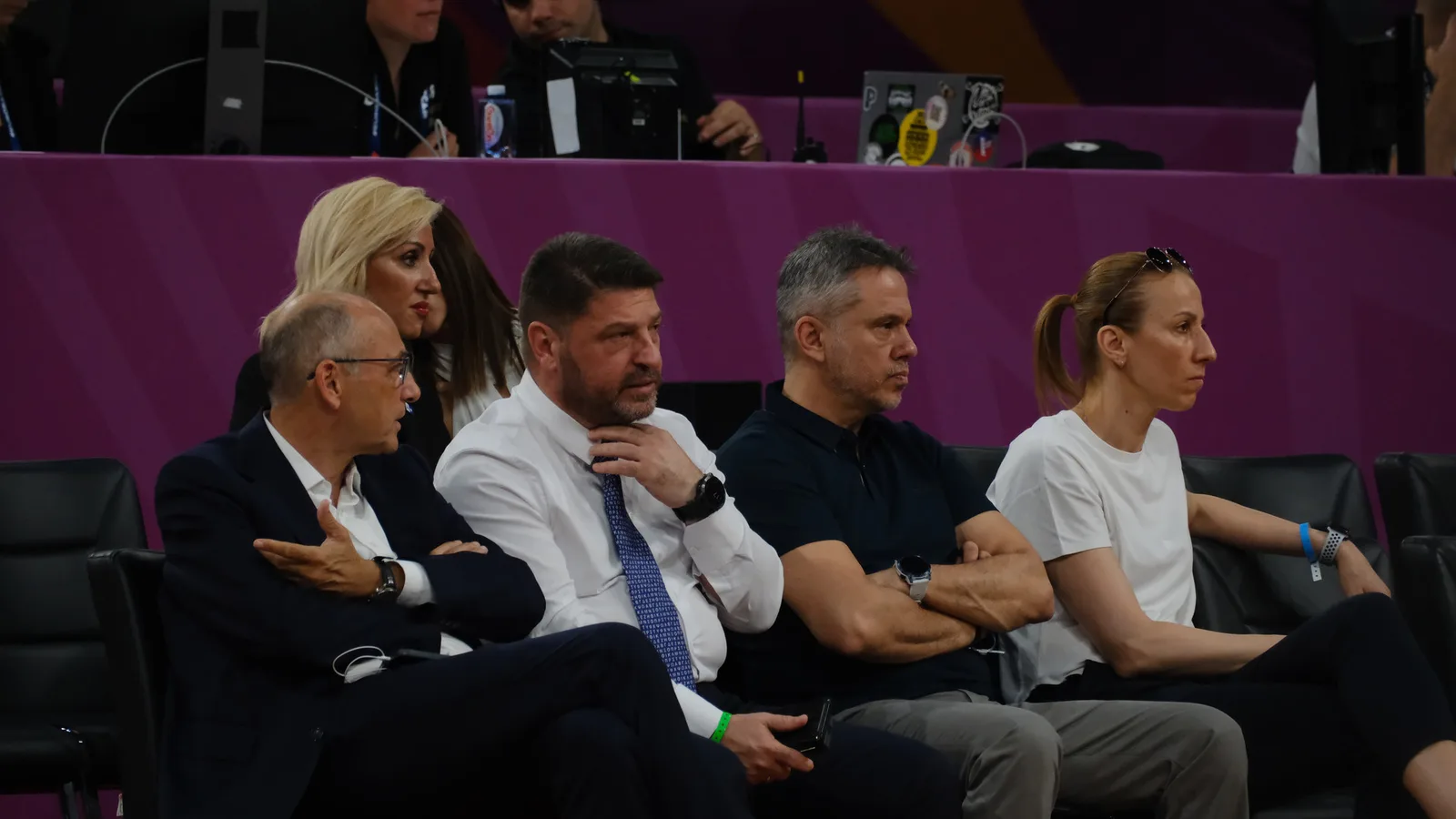 Архив: Вангелис Лиолиос (вляво, с очила) на трибуните на Евробаскет за жени, 27 юни 2025 г.; останалите зрители не са идентифицирани като участници в разследването. Не е кадър от арестите. Zafer / Wikimedia Commons, CC BY 4.0; изрязано до 16:9. https://commons.wikimedia.org/wiki/File:Vangelis_Liolios_-_George_Dikeoulakos_20250627.jpg ; https://creativecommons.org/licenses/by/4.0/