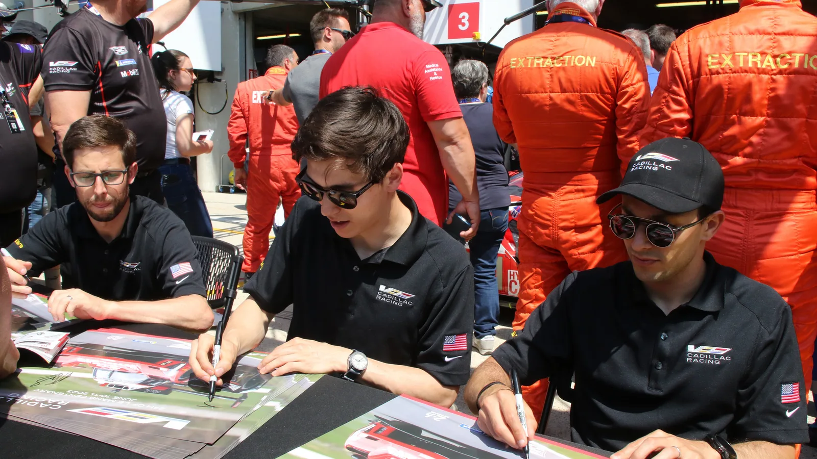 Архивен кадър: Джак Ейткен (в центъра) с пилотите на Cadillac Racing по време на среща с фенове в Льо Ман през 2023 г.; не е снимка от „Пти Льо Ман“ 2026 г. Martin Lee / Wikimedia Commons, CC BY-SA 2.0; изрязано до 16:9. Оригинал: https://commons.wikimedia.org/wiki/File:Alexander_Sims,_Jack_Aitken_%26_Luis_Felipe_Derani_-_Cadillac_V-Series.R_Hybrid_during_the_pitwalk_at_the_2023_Le_Mans_(53467916736).jpg ; лиценз: https://creativecommons.org/licenses/by-sa/2.0/ ; преработката е под CC BY-SA 2.0.