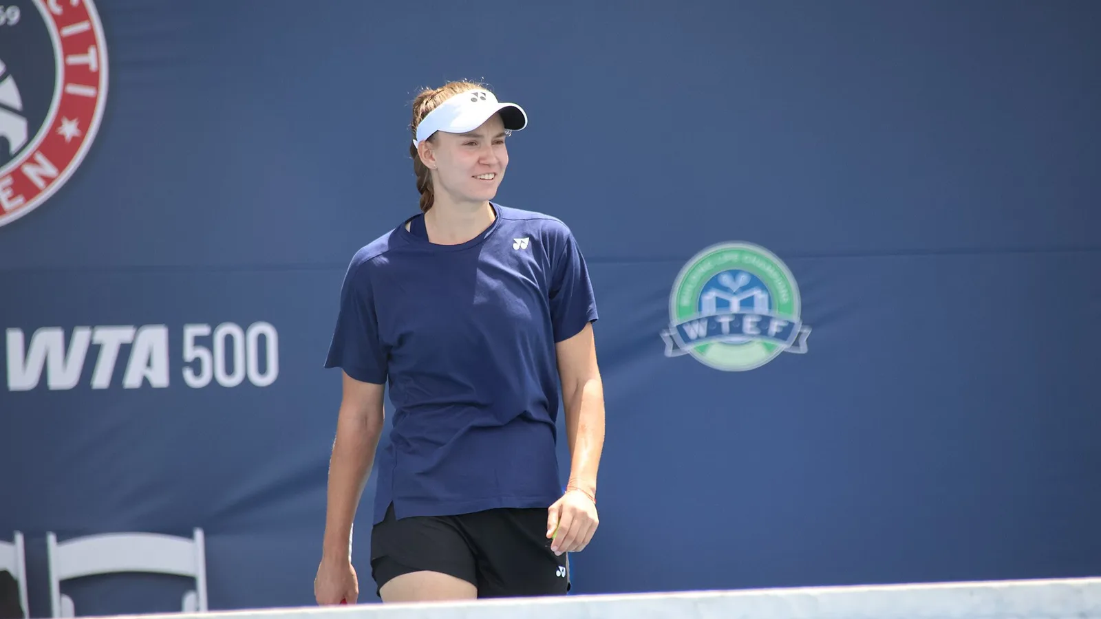 Архив: Елена Рибакина на тренировка преди Washington Open, 19 юли 2025 г.; не е кадър от Токио 2026 или контузията. Hameltion / Wikimedia Commons, CC BY-SA 4.0. https://commons.wikimedia.org/wiki/File:Elena_Rybakina_(2025_DC_Open)_05.jpg ; https://creativecommons.org/licenses/by-sa/4.0/ ; изрязано и преоразмерено до 16:9 без AI редакция, адаптация под същия лиценз.