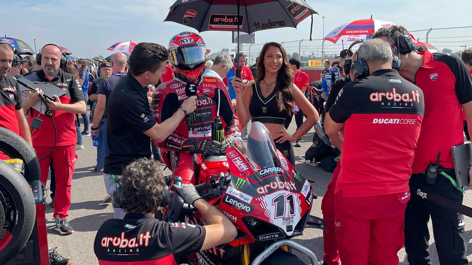 Николо Булега с Ducati Panigale V4 R №11 преди старт на WorldSBK в Кремона през 2024 г. — архивен кадър, не от петъчните тренировки в Ещорил през 2026 г. Vale93b / Wikimedia Commons, CC BY-SA 4.0; изрязано до 16:9. Оригинал: https://commons.wikimedia.org/wiki/File:N.Bulega_Cremona_Circuit_WSBK_2024.jpg ; лиценз: https://creativecommons.org/licenses/by-sa/4.0/ ; производната остава под CC BY-SA 4.0.