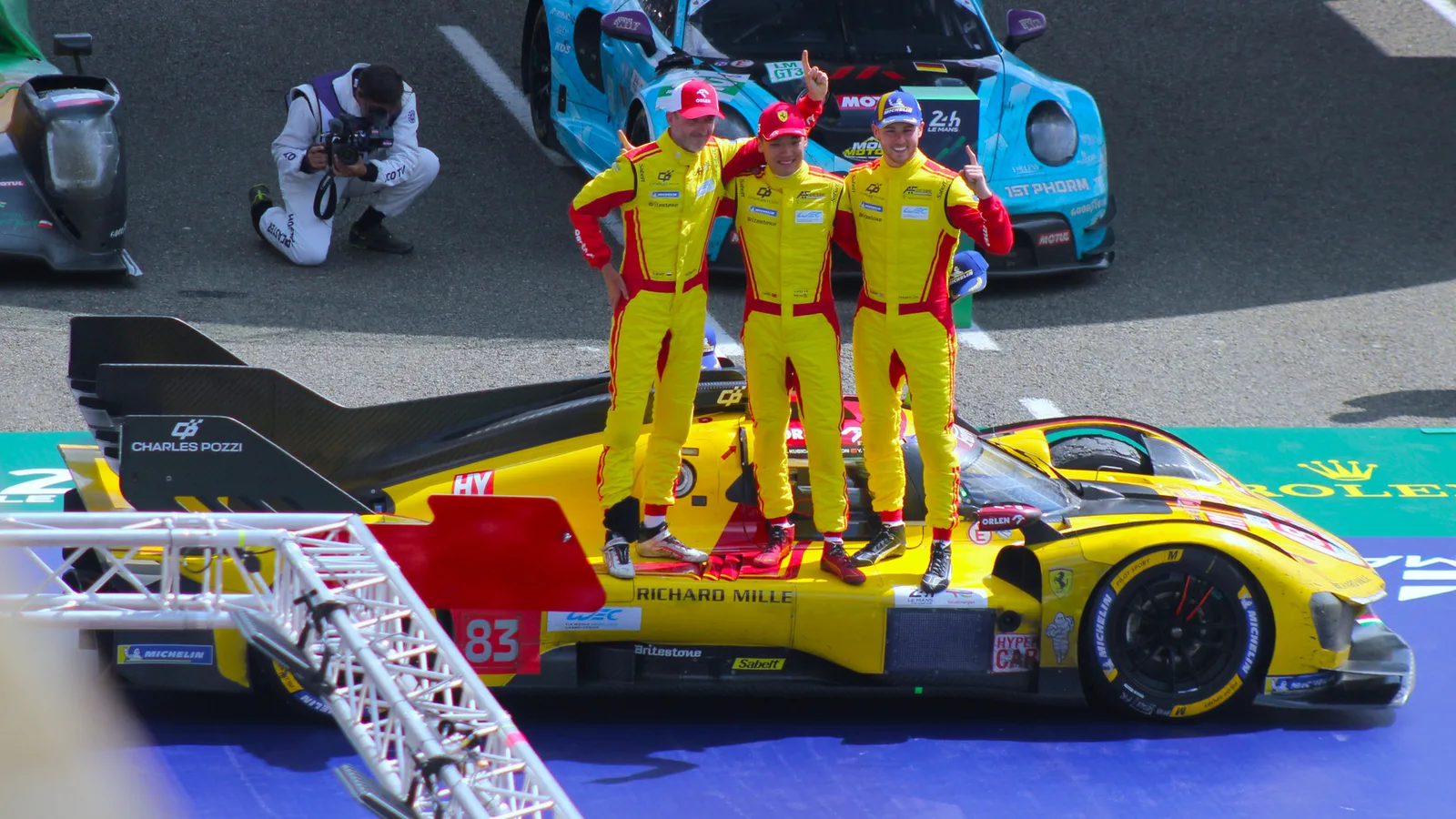 Архив: Роберт Кубица (вляво) с екипажа на Ferrari №83 след победата в Льо Ман на 15 юни 2025 г.; не е кадър от сезон 2026. Lukas Raich / Wikimedia Commons, CC BY-SA 4.0; изрязано и оразмерено до 16:9, адаптация под същия лиценз. Оригинал: https://commons.wikimedia.org/wiki/File:24H_Le_Mans_2025_Winning_picture_of_car_83.jpg ; лиценз: https://creativecommons.org/licenses/by-sa/4.0/