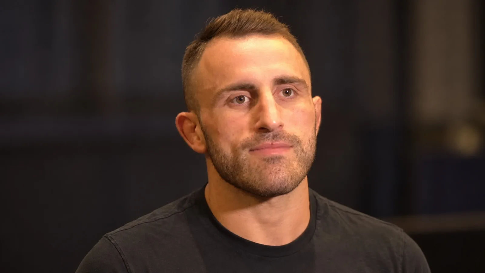 Александър Волкановски — AI адаптация на архивен портрет от UFC 232 (2018), не кадър от UFC 333. MMAnytt / Wikimedia Commons, CC BY 3.0: https://creativecommons.org/licenses/by/3.0/ . Оригинал: https://commons.wikimedia.org/wiki/File:Alexander_Volkanovski_at_UFC_232.jpg ; променени фон и кадриране чрез image-to-image.