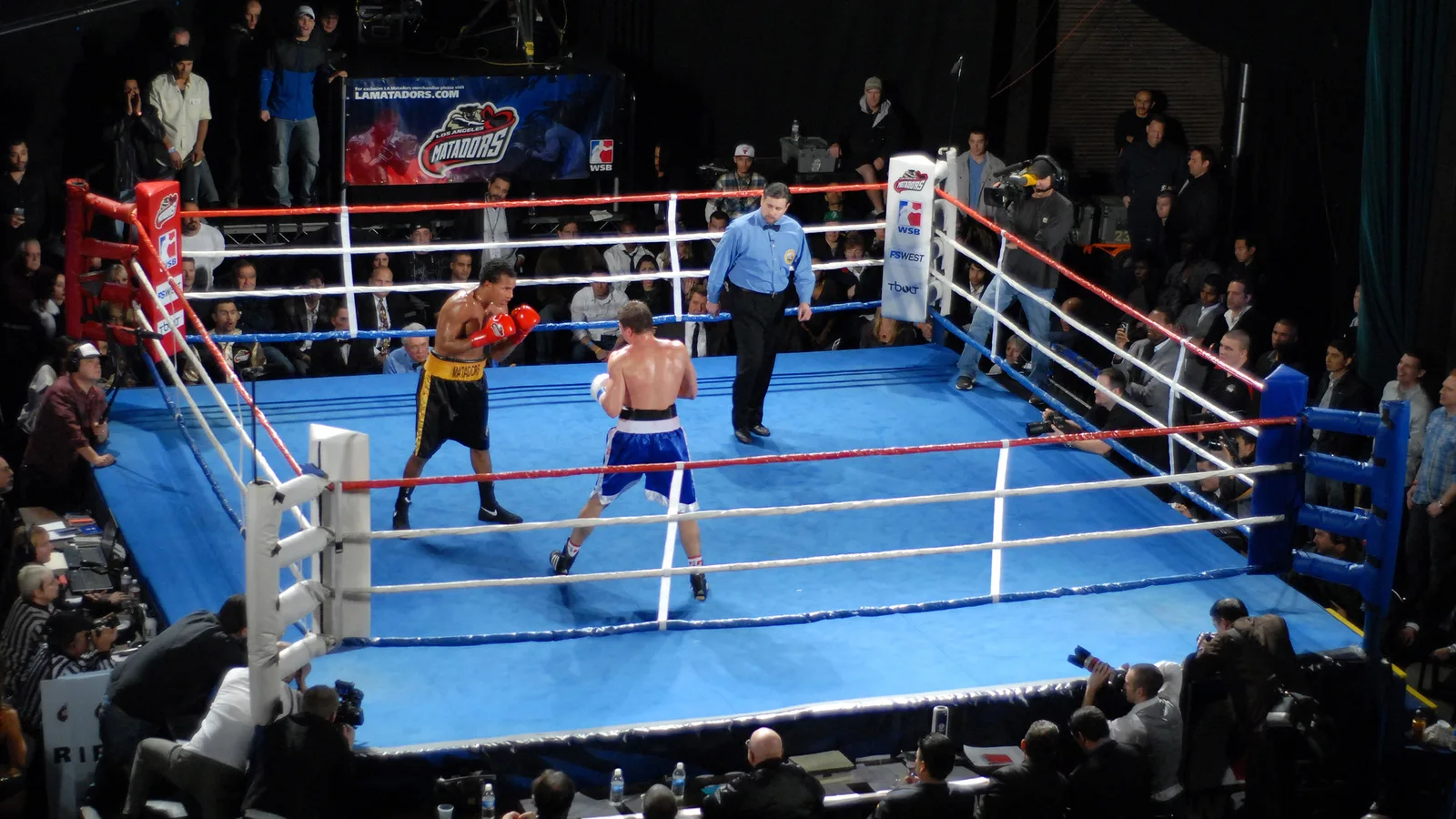 Архивен боксов двубой от World Series of Boxing, Лос Анджелис Матадорс – Москва Динамо, Холивуд, 4 декември 2011 г.; не показва Fame Fighting 4 или неговите участници. © Glenn Francis, www.PacificProDigital.com / Wikimedia Commons, CC BY-SA 3.0; изрязано до 16:9, адаптацията е под същия лиценз. Оригинал: https://commons.wikimedia.org/wiki/File:World_Series_Boxing_Ring.JPG ; лиценз: https://creativecommons.org/licenses/by-sa/3.0/