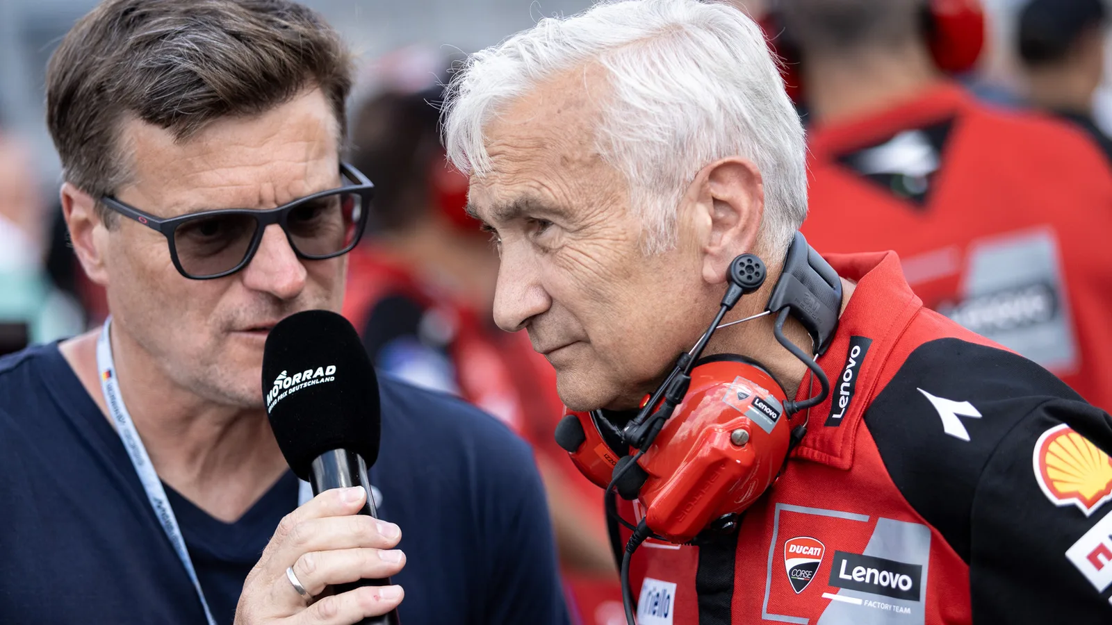 Давиде Тардоци (вдясно), мениджър на Ducati, в интервю на Гран при на Германия през юли 2026 г. — архивна снимка, не от Мандалика. #TeamEG00 / Wikimedia Commons; авторски Public Domain Mark, потвърден от FlickreviewR 2. Оригинал: https://commons.wikimedia.org/wiki/File:Davide_Tardozzi_at_the_2026_German_motorcycle_Grand_Prix.jpg ; https://www.flickr.com/photos/estrellagalicia00/55391488299/ ; изрязано до 16:9 без генеративна промяна.