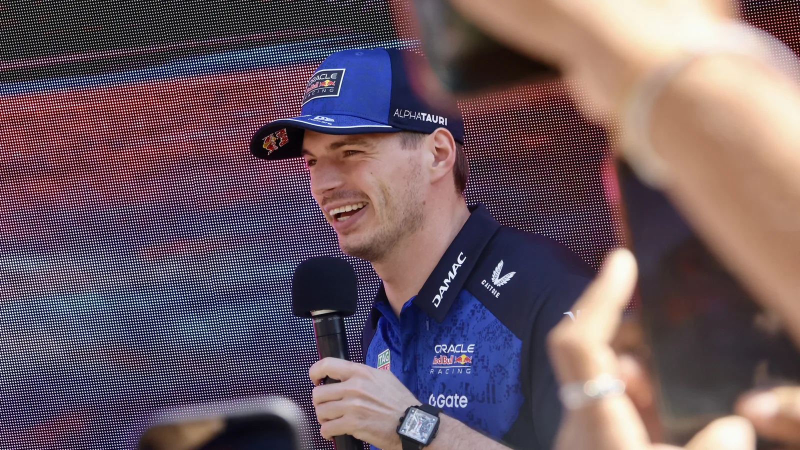 Макс Верстапен говори с микрофон на събитие на Red Bull в Мелбърн на 5 март 2026 г. — архивна снимка, не от състезанието. Yu Chu Chin / Wikimedia Commons, CC BY-SA 4.0; изрязана до 16:9. Оригинал: https://commons.wikimedia.org/wiki/File:Max_Verstappen_at_the_Red_Bull_Fan_Zone_%E2%80%93_Crown_Riverwalk,_Melbourne_(028A7663).jpg ; лиценз: https://creativecommons.org/licenses/by-sa/4.0/ ; производното изображение е под CC BY-SA 4.0.